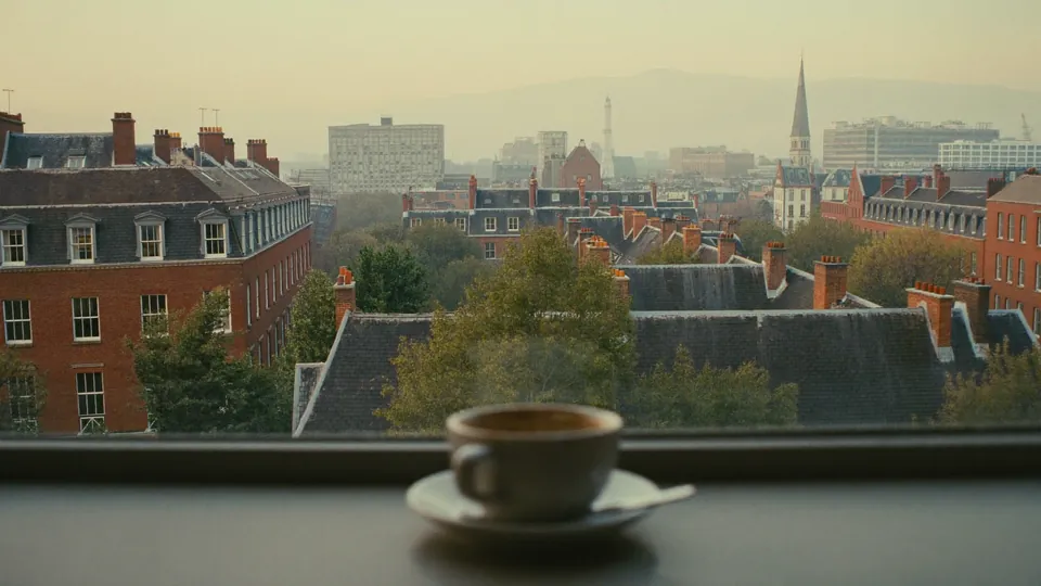 An illustrative view over the rooftops of a British city at dawn from an office window