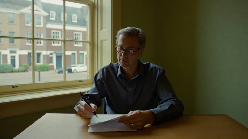 An illustrative adviser reading a printed report at a desk by a tall sash window